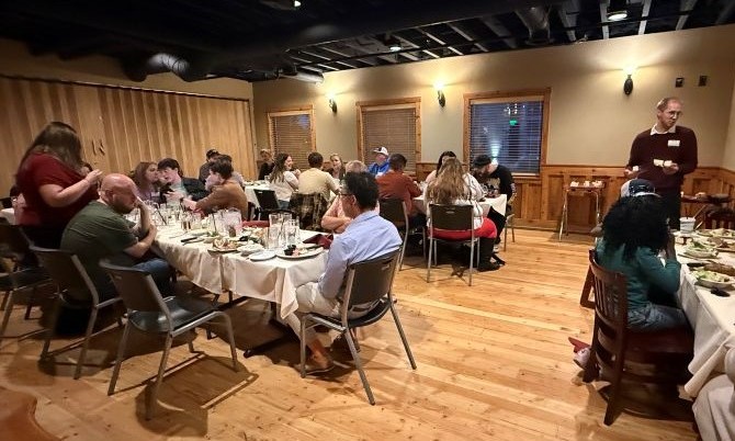 A group of people dining and socializing at tables in a warmly lit event space.